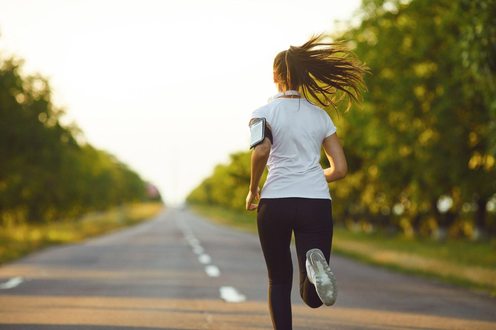 Runner with a phone armband jogging along a tree-lined road at sunset