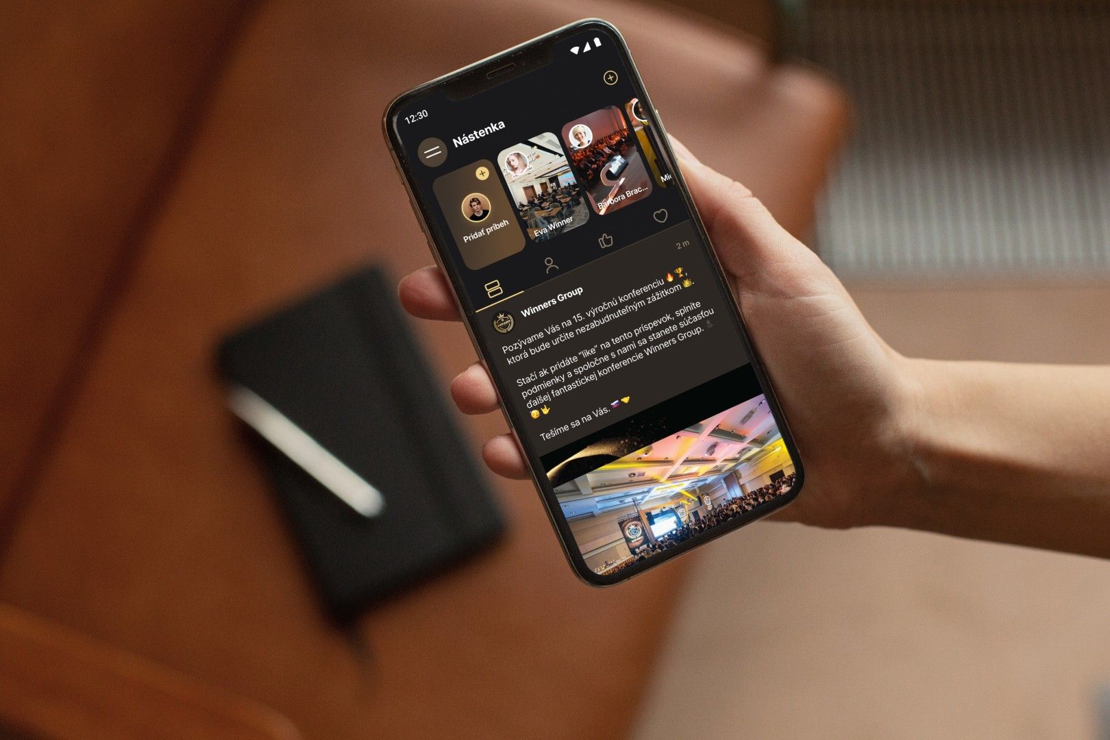 Person holding a phone showing the broker app social feed